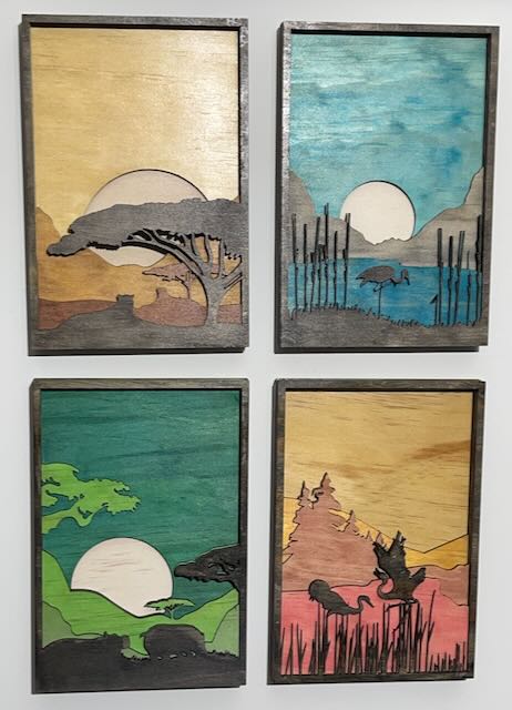 This image shows four laser-cut wooden panels, each depicting a nature scene with a silhouetted foreground and a vibrant, painted background. The panels feature various landscapes, including savannas, wetlands, forests, and mountain ranges. The sun or moon appears in the background, creating a stunning contrast between light and shadow. Each scene is beautifully layered, with intricate cutouts that bring depth and dimension to the artwork, making it an eye-catching and elegant representation of nature's beauty. laser cutting