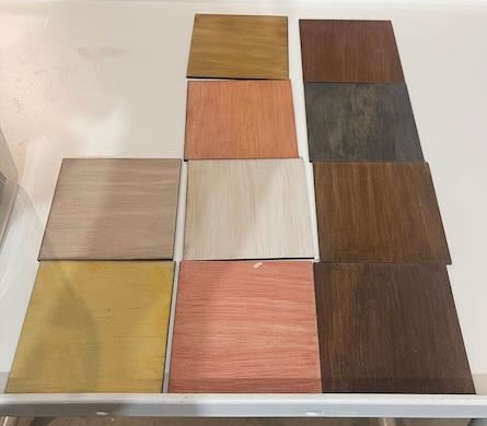 This image features a selection of color samples, each piece a small square of wood in different shades and finishes. The arrangement showcases various tones, ranging from lighter natural woods to deeper, richer hues like oak, mahogany, and dark walnut. Each square is placed neatly on a white surface, forming a grid-like pattern, offering a clear visual contrast between the wood stains and finishes, perfect for helping customers choose the best material for their laser cutting or crafting projects.